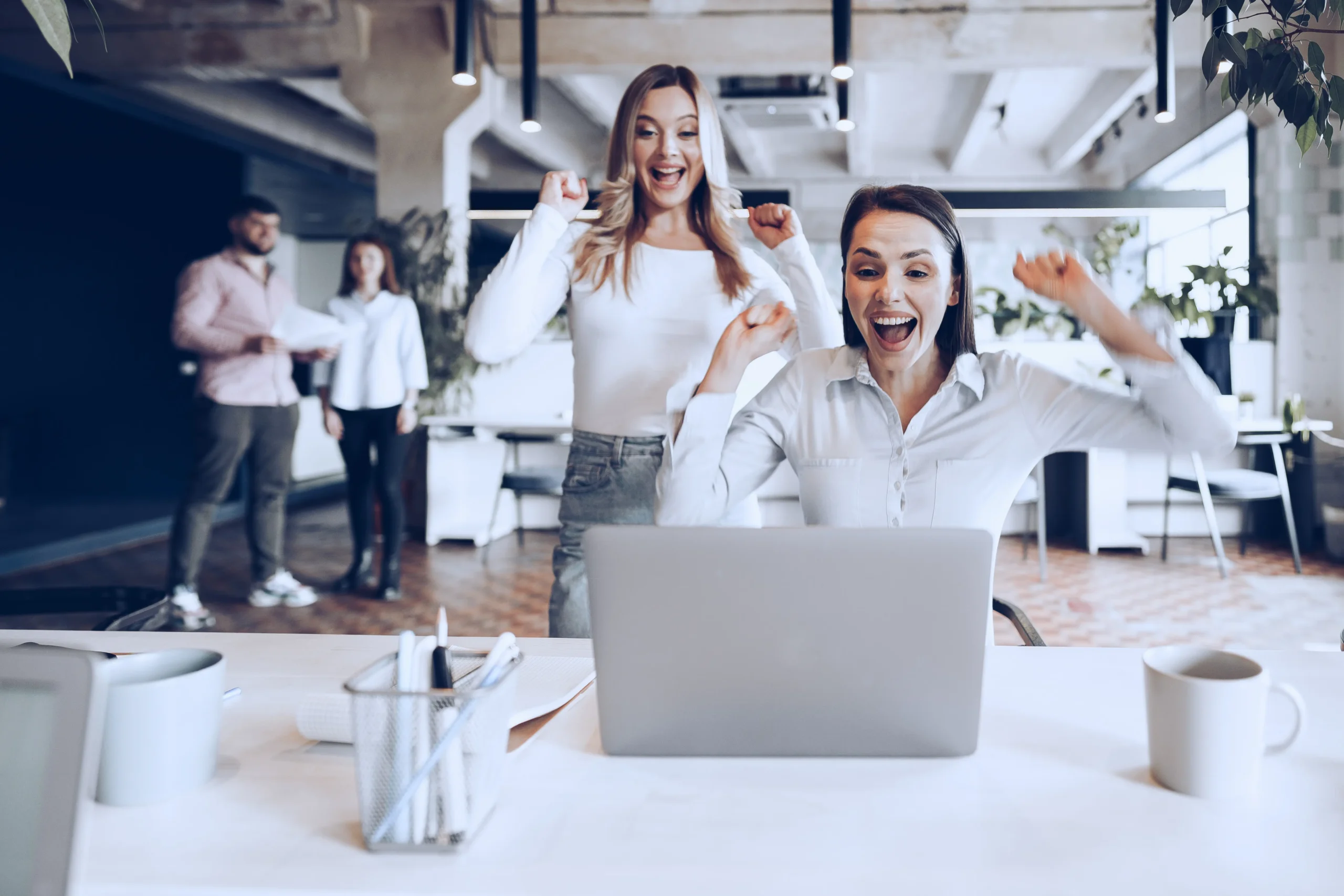 two young happy businesswomen celebrating project success office scaled Interwebsite Webbyrå